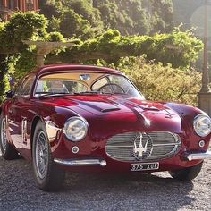 an old red sports car is parked on the gravel