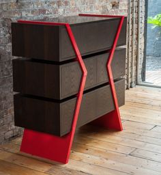 an unusual wooden table with red accents on the top and bottom, in front of a brick wall