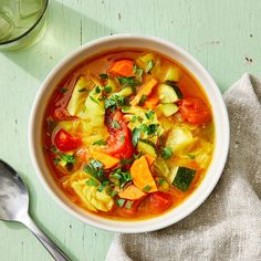 a white bowl filled with vegetable soup on top of a green table next to a spoon