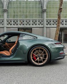 a green sports car parked in front of a building with its door open and the driver's seat up