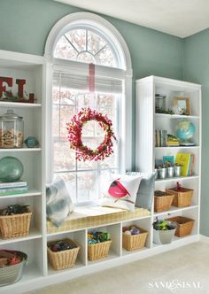 a window seat in front of a white book shelf filled with books and other items