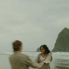 two people are walking on the beach near the water and one is holding his hand