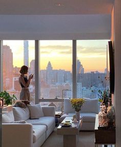 a woman standing in front of a window looking at her cell phone while she stands on the couch