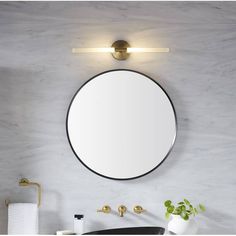 a round mirror mounted on the wall above a sink in a bathroom with gold faucet