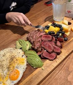 a wooden cutting board topped with steak, eggs and fruit