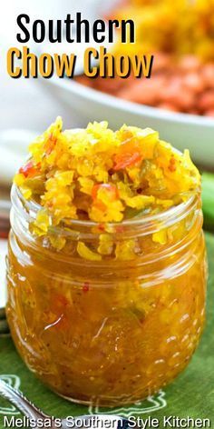 a glass jar filled with yellow and red food next to a plate of carrots