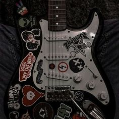 an electric guitar with many stickers on it's body and neck, sitting in someones lap