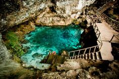 stairs lead down to a blue pool in the middle of a rocky area with clear water