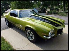 a green muscle car parked in front of a house