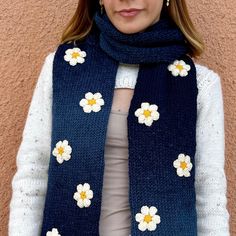 a woman wearing a blue scarf with white flowers on it, standing in front of a wall