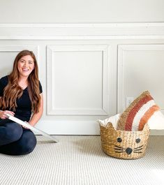 a woman sitting on the floor next to a basket with a cat face drawn on it