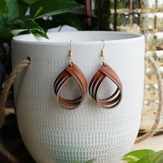 a pair of brown leather earrings sitting on top of a white vase