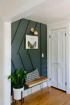 a room with a bench and some plants on the wall in front of it that is painted dark green