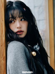 a woman with long black hair leaning against a wooden wall and looking at the camera