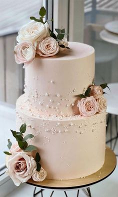 a three tiered wedding cake with pink roses on top and white flowers on the side