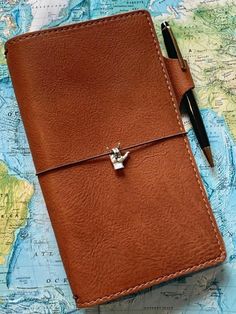 a brown leather notebook with a pen on top of it and a map in the background