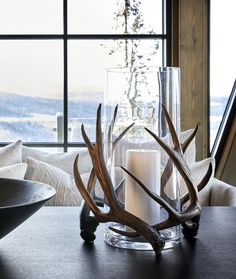 a candle is sitting on a table with antlers in front of a large window