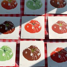 six different colored tomatoes on white cards sitting on a red and green checkered tablecloth