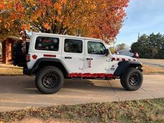 a white jeep parked in front of a tree with red and orange leaves on it