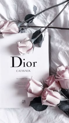 the book dior gatwalk is laying on a white sheet with pink roses