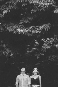 a man and woman standing next to each other in front of some trees with their eyes closed