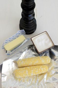 corn on the cob and butter sitting on top of aluminum foil next to an oven