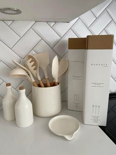 kitchen utensils in white ceramic containers next to a cardboard box on a counter