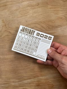 a person holding up a calendar sticker on top of a wooden table