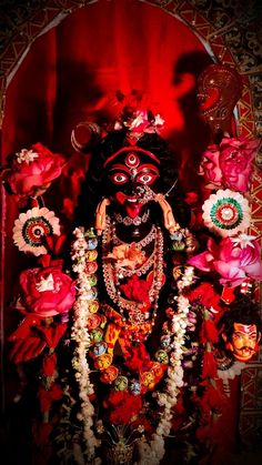 an idol is displayed in front of a red wall with flowers and other decorations on it