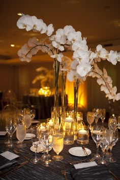 there are many flowers in the vases on the table with wine glasses and silverware