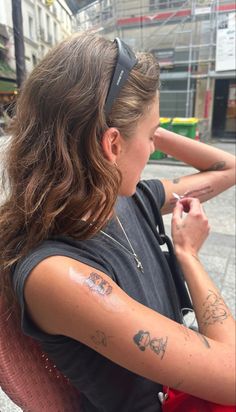 a woman with tattoos on her arm sitting in a chair and writing on her arm