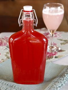 a red bottle sitting on top of a table next to a glass filled with liquid