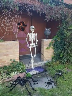 halloween decorations in front of a house with spider webs on the ground and two fake skeletons