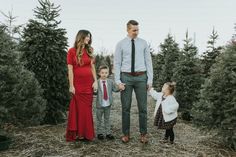 a man and woman holding hands with two small children in front of christmas tree trees