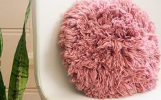 a pink fuzzy ball sitting on top of a white chair next to a potted plant