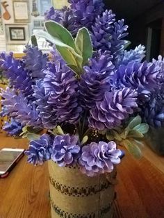 a vase filled with purple flowers sitting on top of a wooden table next to a cell phone