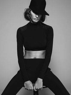 a woman sitting on top of a stool wearing a hat and black pants with her hands in her pockets