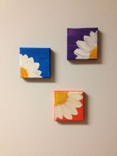 three square paintings with white and yellow flowers painted on them, hanging on the wall