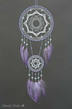 a purple and white dream catcher hanging from a hook on a gray wall with beads