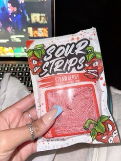 someone holding up a package of sour strips in front of a computer keyboard and monitor