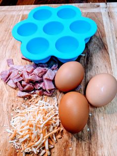 eggs, ham and grated cheese on a cutting board next to an egg tray