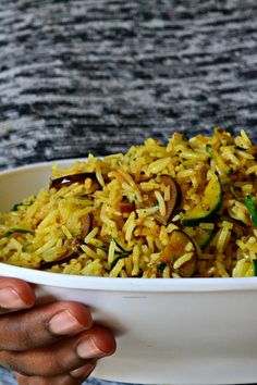 a person holding a white bowl filled with rice and veggies on the side