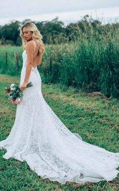 a woman in a white wedding dress holding a bouquet and looking down at the ground