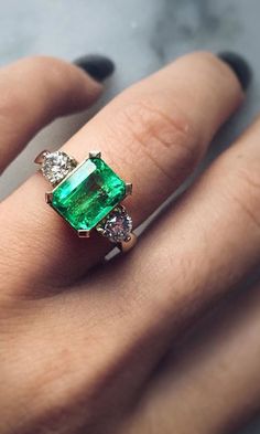 a woman's hand holding an emerald and diamond ring