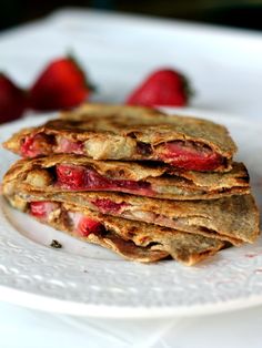 a stack of crepes with strawberries on the side sitting on a white plate