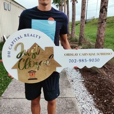 a man holding up a sign that says, the capital realty is open and it's in front of some palm trees