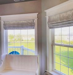 a window seat in the corner of a room with two windows overlooking a grassy field