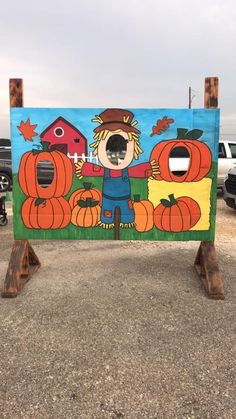 a painted sign in the middle of a parking lot with pumpkins and a scarecrow on it