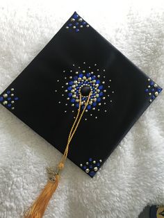 a black graduation cap with blue beads and tassels on the side, laying on a white blanket