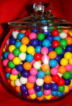 a large glass jar filled with lots of colorful candy balls on a red cloth background